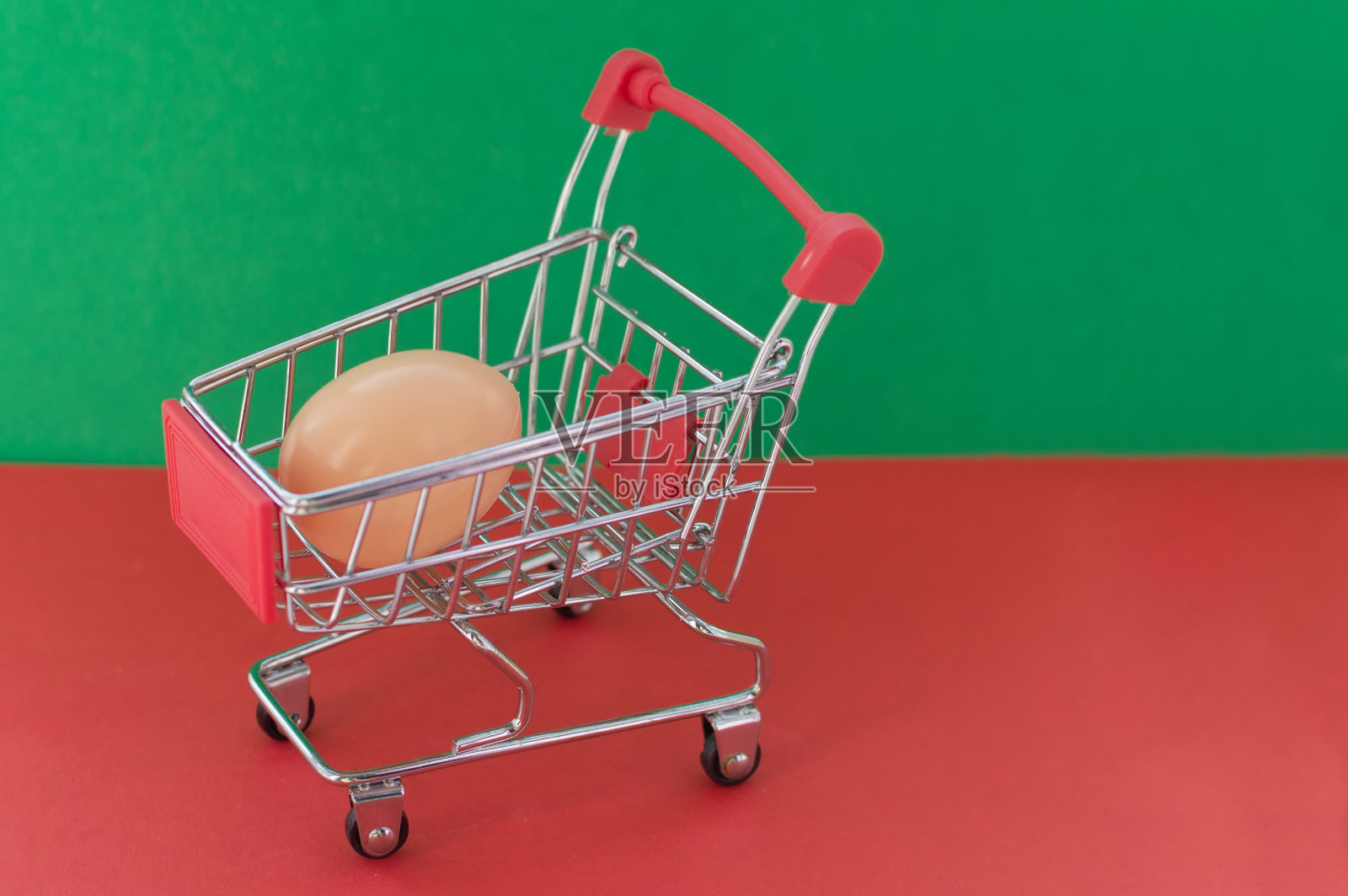 红色和绿色背景的购物车，里面有一个塑料鸡蛋。含有有害添加剂的非天然产品的概念。照片摄影图片