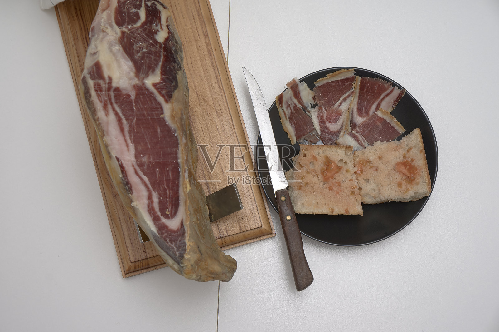 典型的西班牙火腿，刀旁边，面包和番茄在一个黑色的盘子。前视图。照片摄影图片