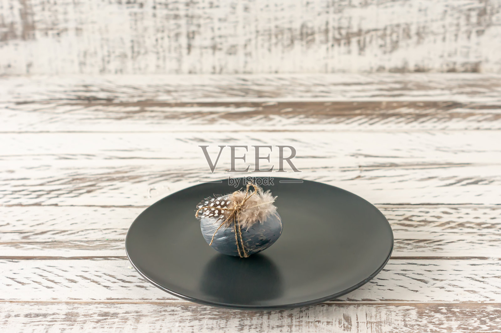 时髦的彩色复活节彩蛋，深色和羽毛的盘子放在木桌上。为复活节假期做准备。Fesstive组成。照片摄影图片