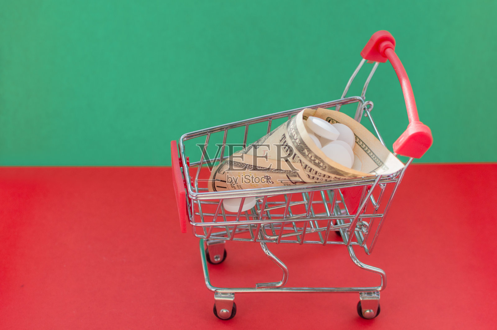 购物车在红色和绿色的背景与药品包裹在钱里面。昂贵治疗的概念。照片摄影图片