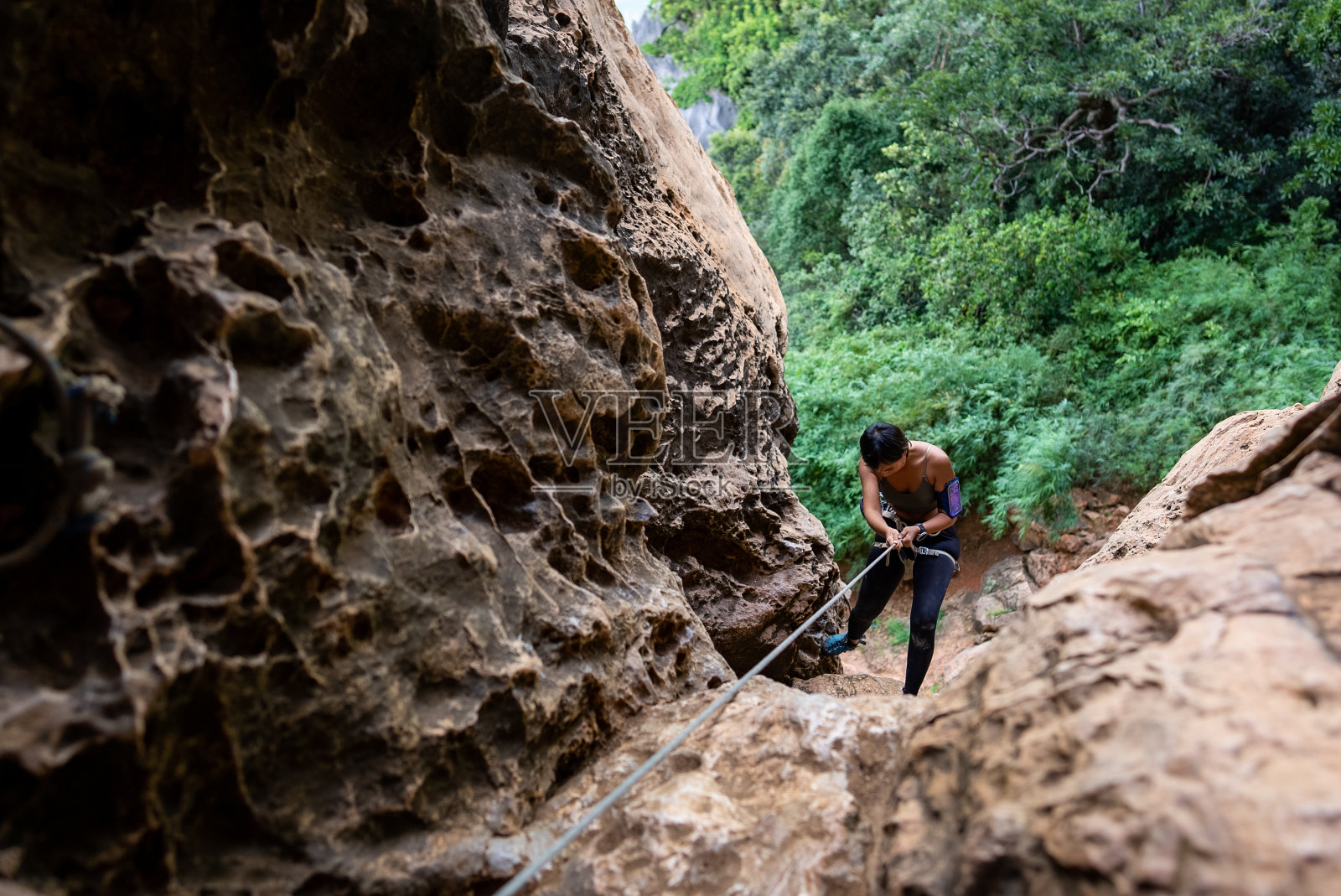 自信的亚洲女攀登者带着安全绳在热带岛屿的岩石山上攀爬。强壮健康的女性，喜欢积极的生活方式和假期极限运动照片摄影图片