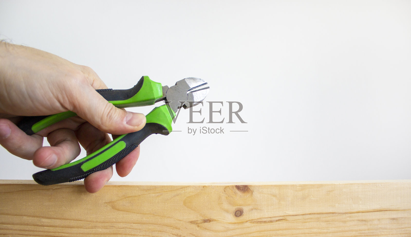 一个男人的手拿着一个放在木棒上的钢丝钳。美丽的白色背景。副本的空间。建筑的概念。照片摄影图片