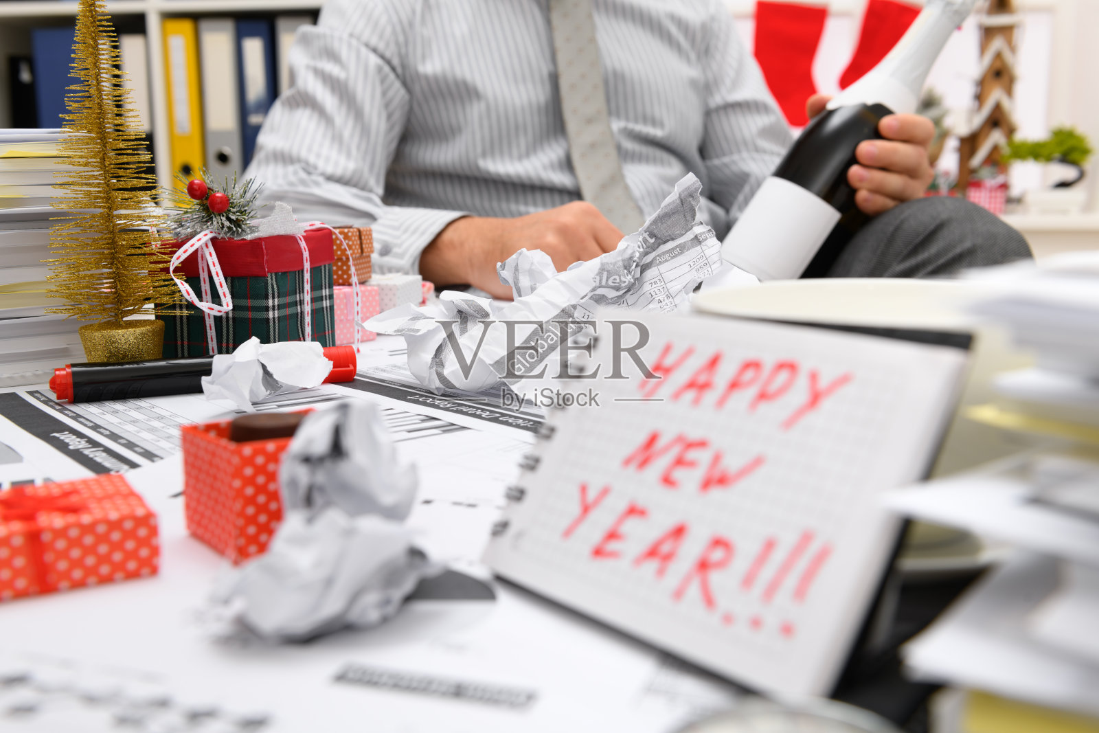 商务节日概念——商人在办公室庆祝新年时装饰圣诞树、糖果等新年装饰品。在记事本上写着新年快乐照片摄影图片