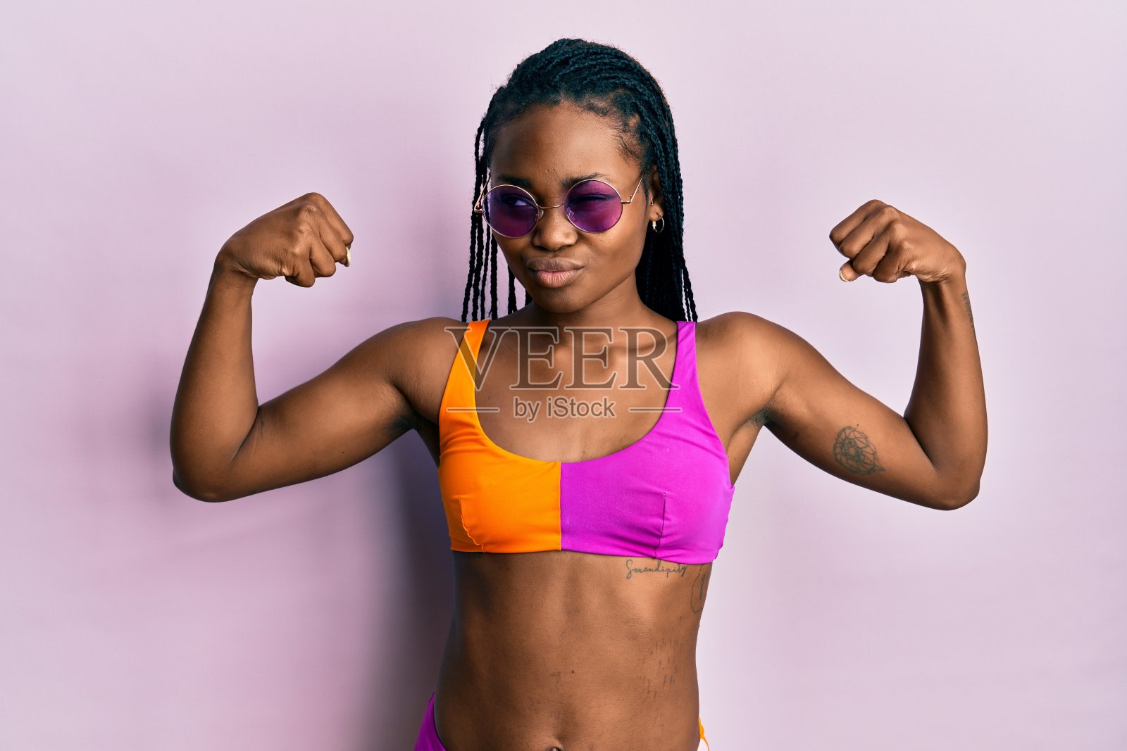 年轻的非洲裔美国妇女穿着比基尼和太阳镜显示手臂肌肉微笑自豪。健康的概念。照片摄影图片