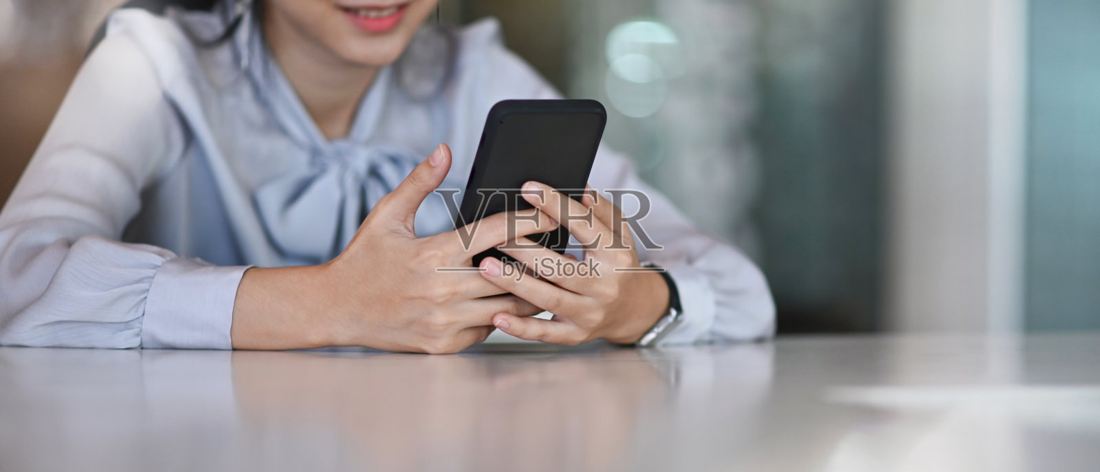 这是一张成功的女商人坐在她的办公桌前使用智能手机的照片。照片摄影图片