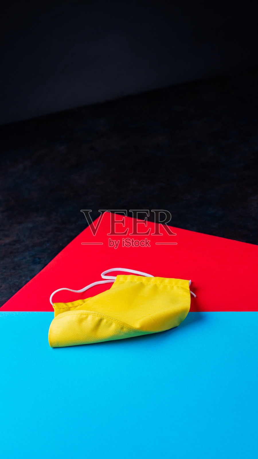 黄色面膜贴在彩色纸上。蓝红色背景的面罩。可重用的防毒面具。本空间照片摄影图片