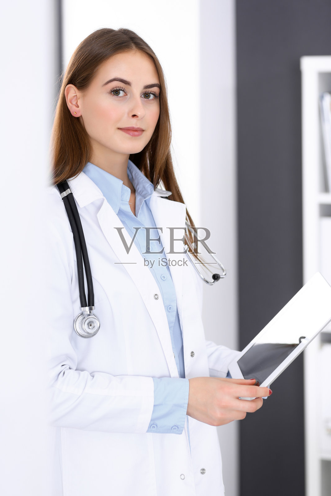 在医院里，一名女医生站在窗边使用平板电脑。快乐的医生在工作。医学保健理念照片摄影图片