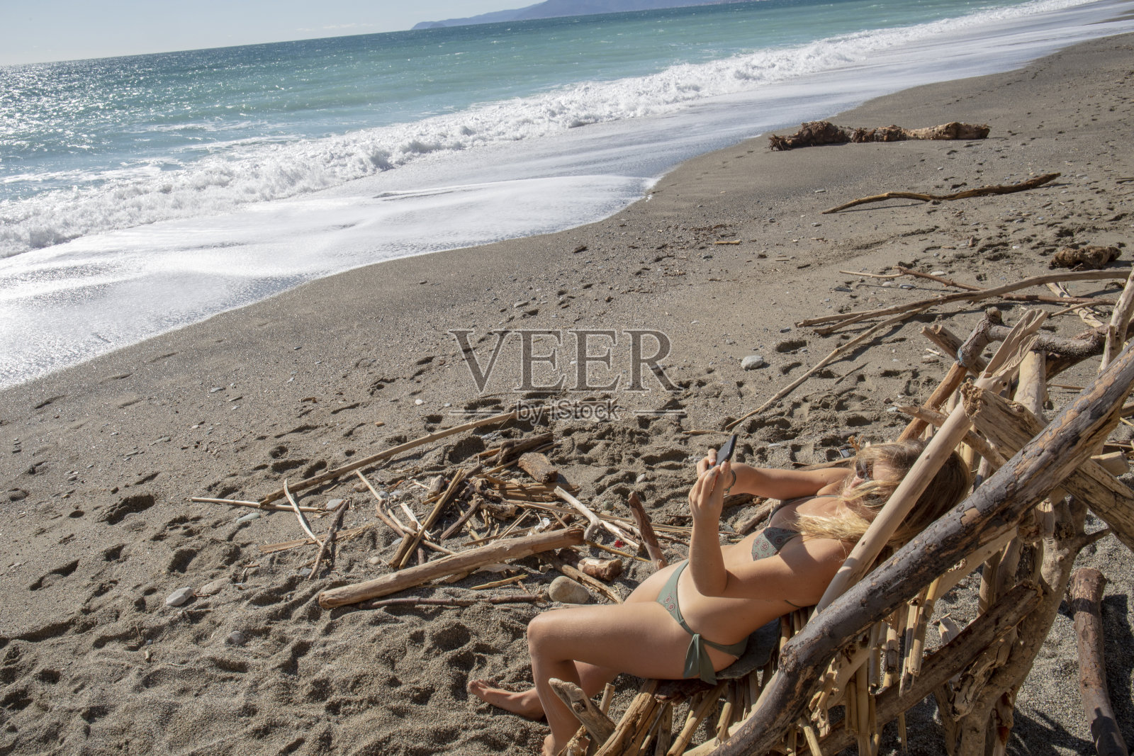 早晨，年轻女子在沙滩上的漂流木椅上放松照片摄影图片