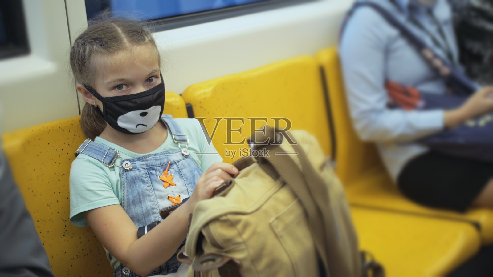 小女孩戴着红色医用防护口罩，乘坐白种人地面列车。飞机上的婴儿。人面具。照片摄影图片