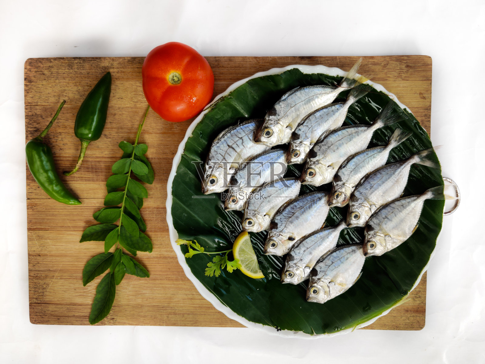 新鲜小马驹鱼的近景装饰与草药和蔬菜在一个木制垫，选择性的焦点。白色背景。照片摄影图片