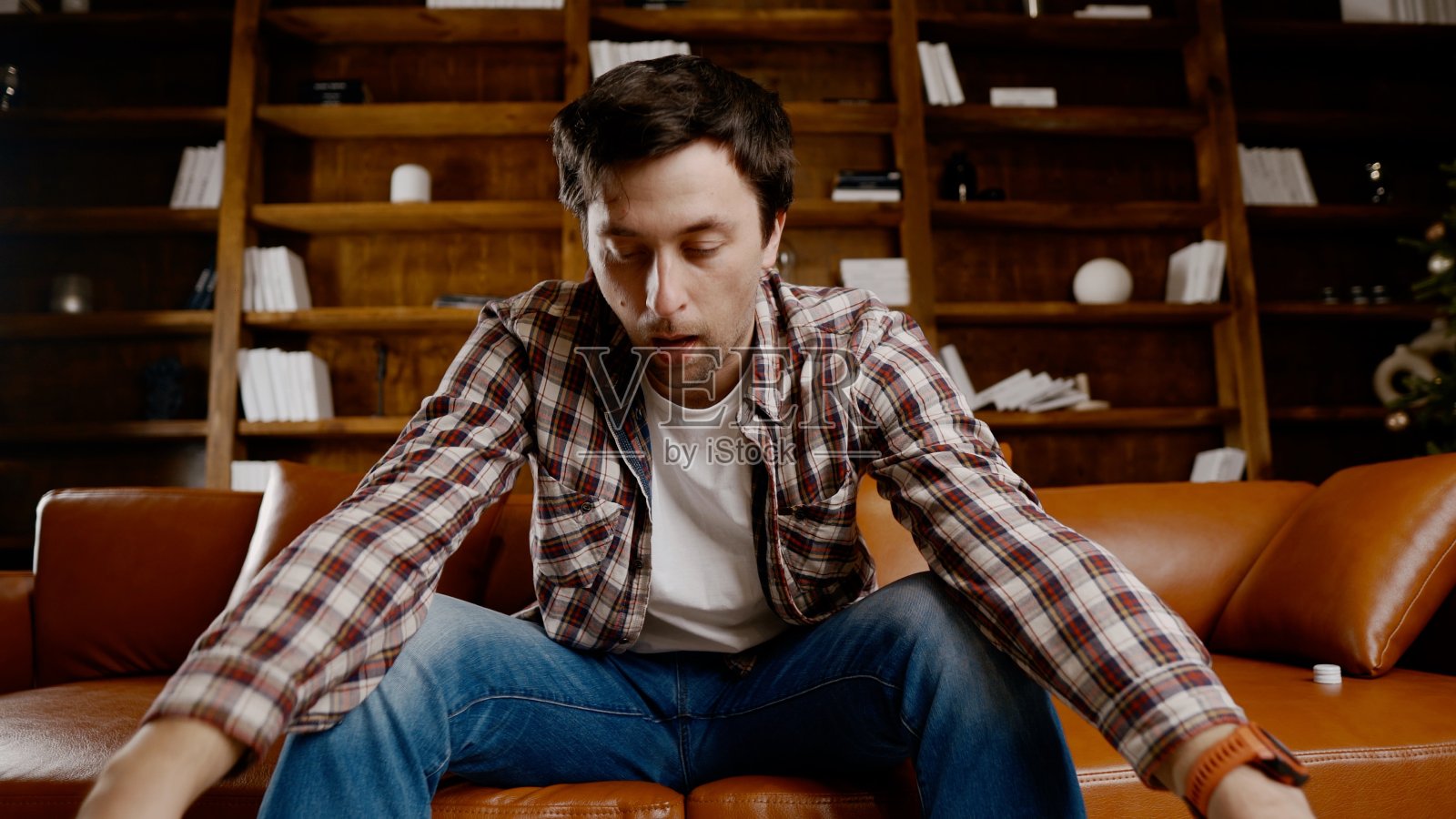 年轻男性酗酒者需要医疗和心理帮助。男人嗜酒成瘾，不能在圣诞节和新年前夜呆在家里的沙发上。一个醉汉在圣诞树旁喝瓶子里的酒照片摄影图片