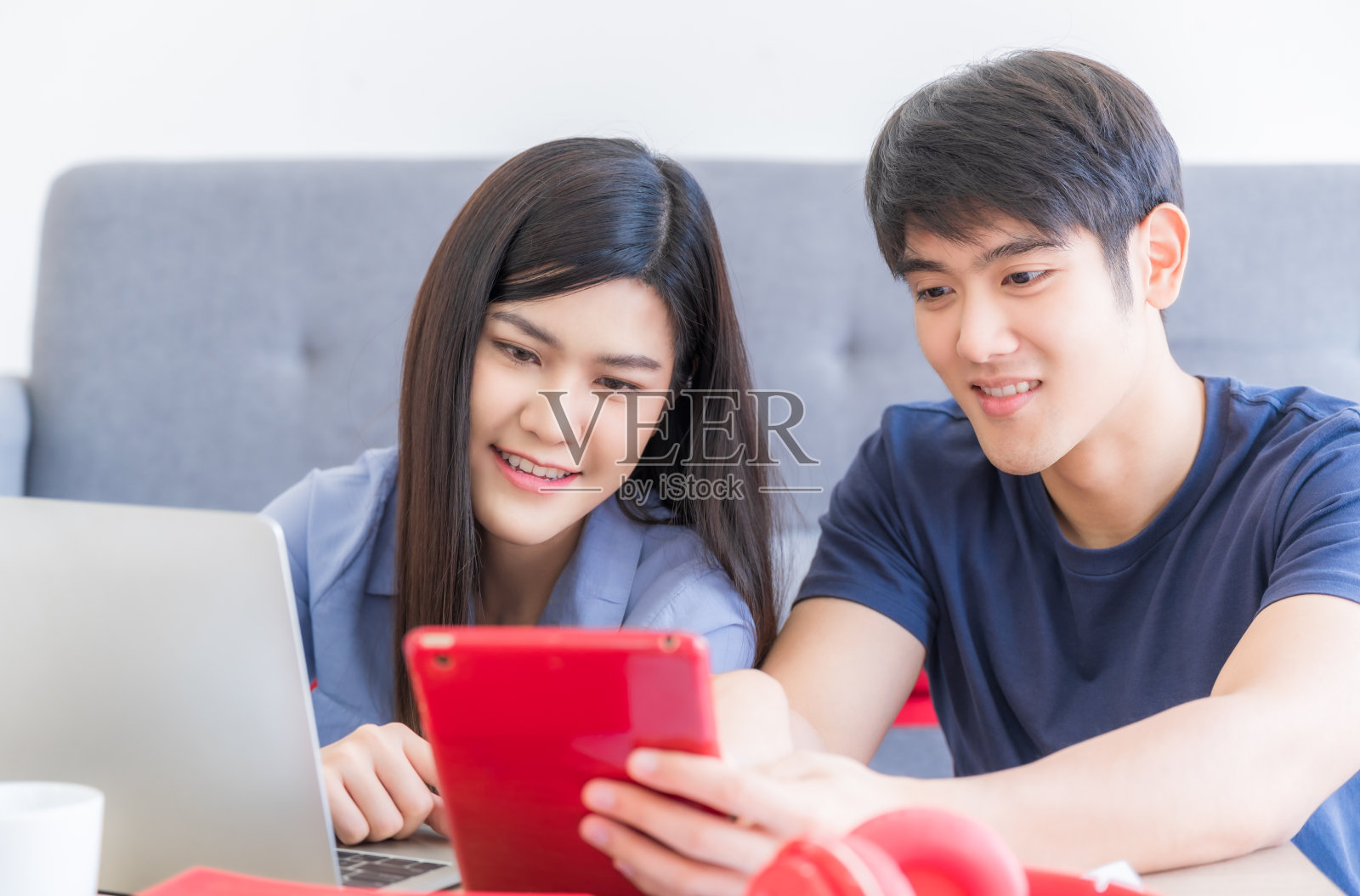 年轻夫妇坐在客厅里，通过智能手机、平板电脑和笔记本电脑进行科技交流照片摄影图片