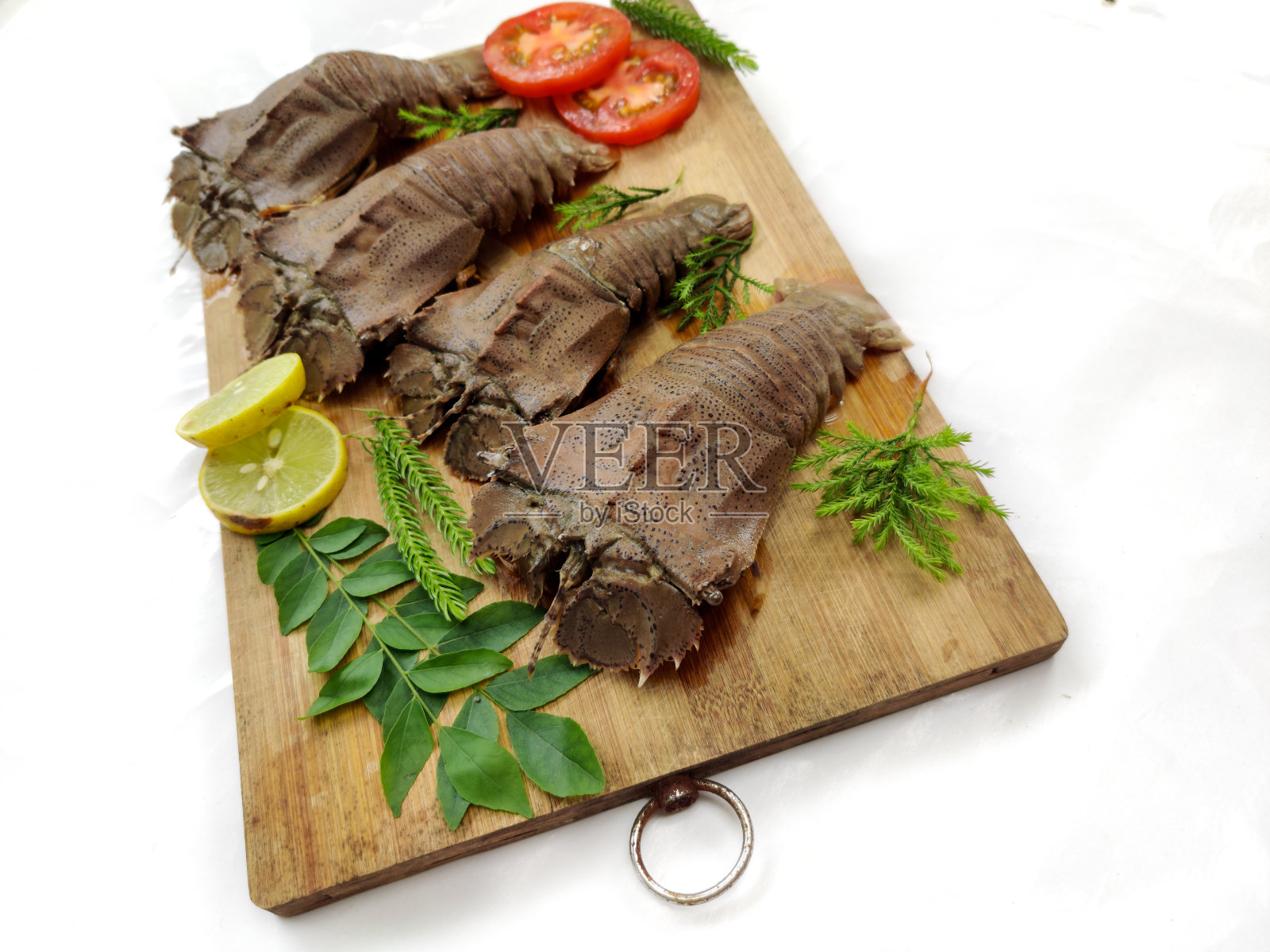 鲜沙龙虾或平头龙虾或拖鞋龙虾(Thenus Orientalis)装饰草本和蔬菜在一个木制垫。白色背景,选择聚焦。照片摄影图片