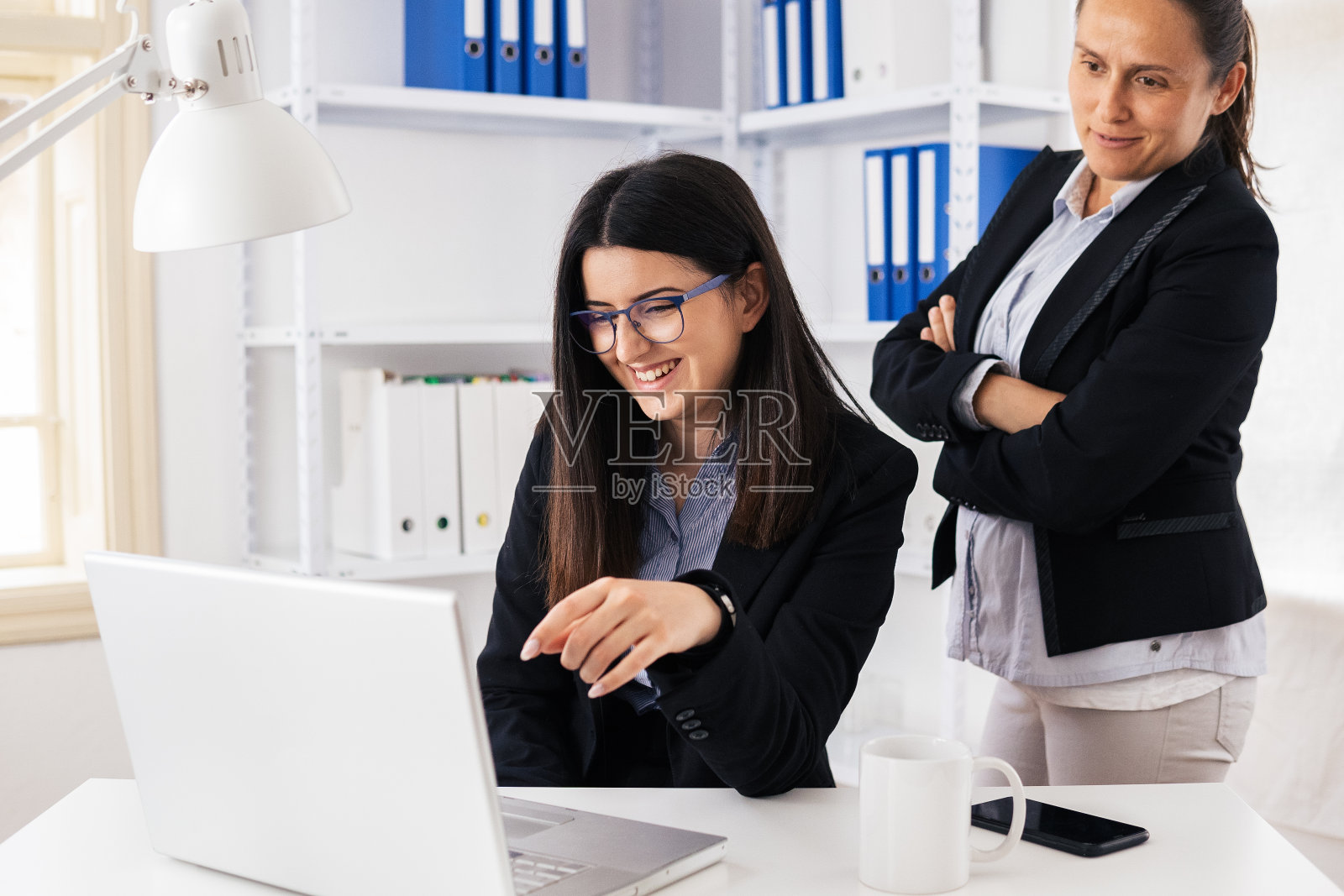 新的标准。新办公室的设置。两名同事在COVID-19大流行期间在办公室共同工作。照片摄影图片