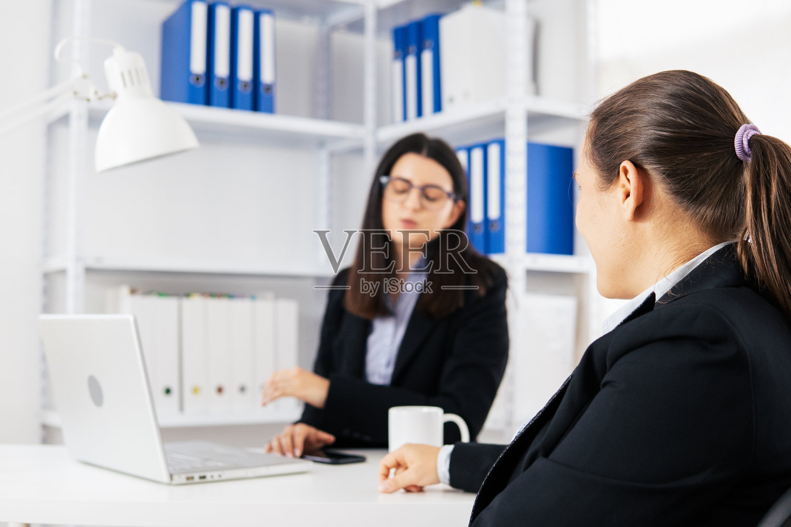 新的标准。新办公室的设置。两名同事在COVID-19大流行期间在办公室共同工作。照片摄影图片