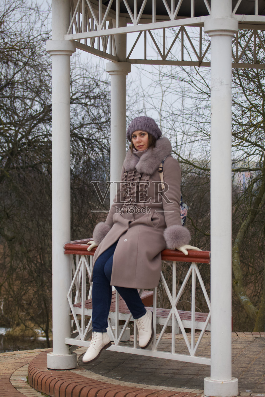 一个穿着冬装的女孩在公园里散步。在凉亭里摆姿势。照片摄影图片
