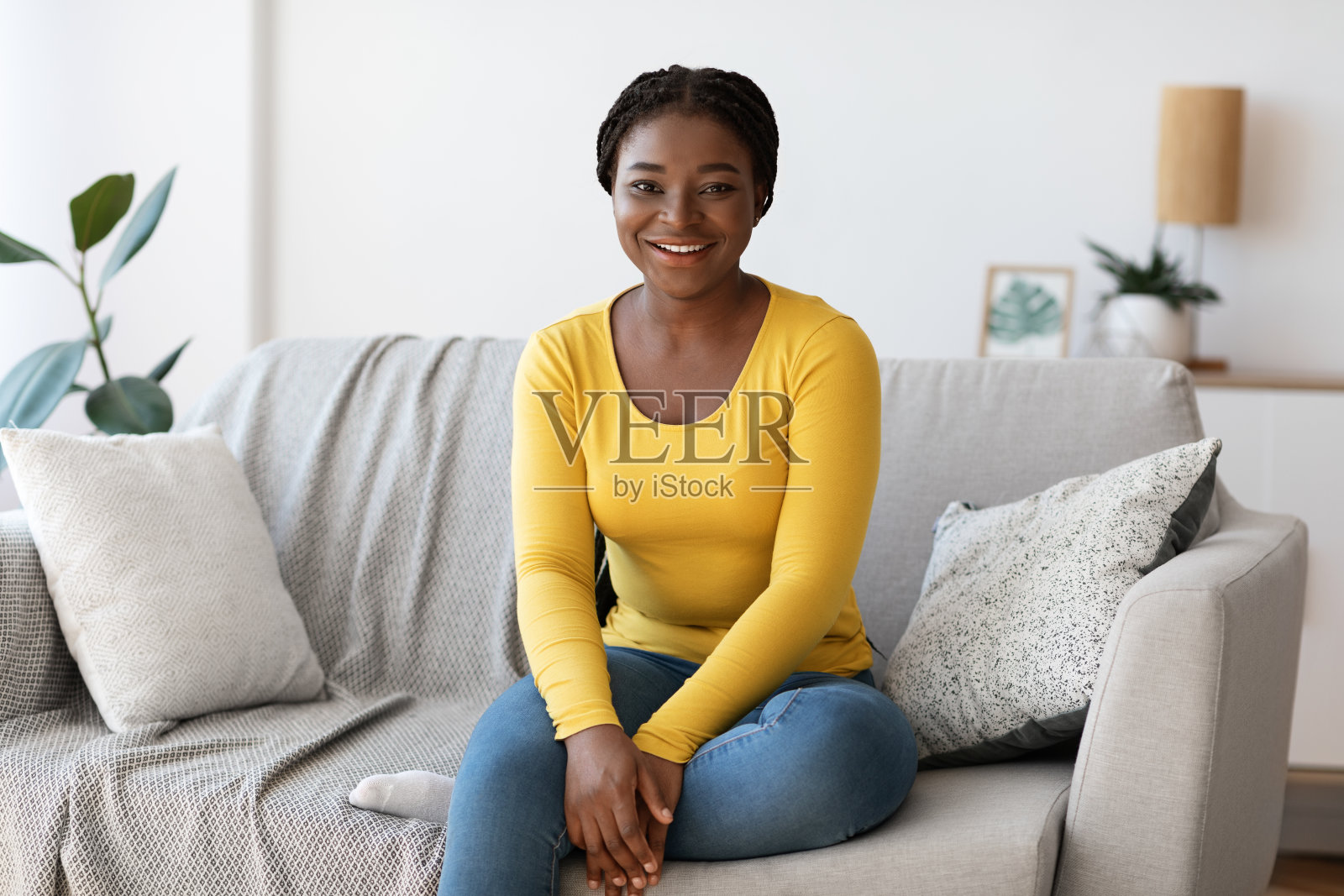 美丽的黑人千禧女性坐在家里的沙发上，对着镜头微笑照片摄影图片