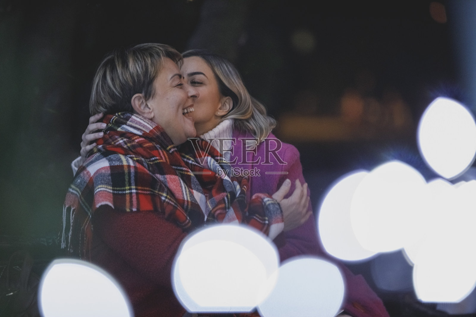 年轻女子拥抱她的母亲，亲吻她的脸颊照片摄影图片