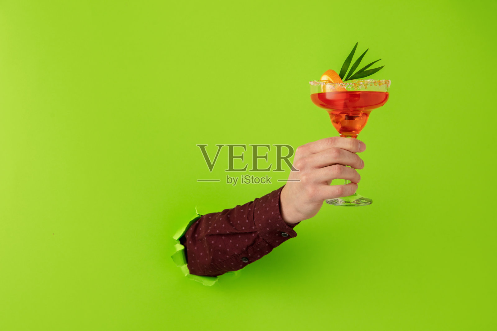 男手拿着鸡尾酒杯打破绿纸背景。照片摄影图片