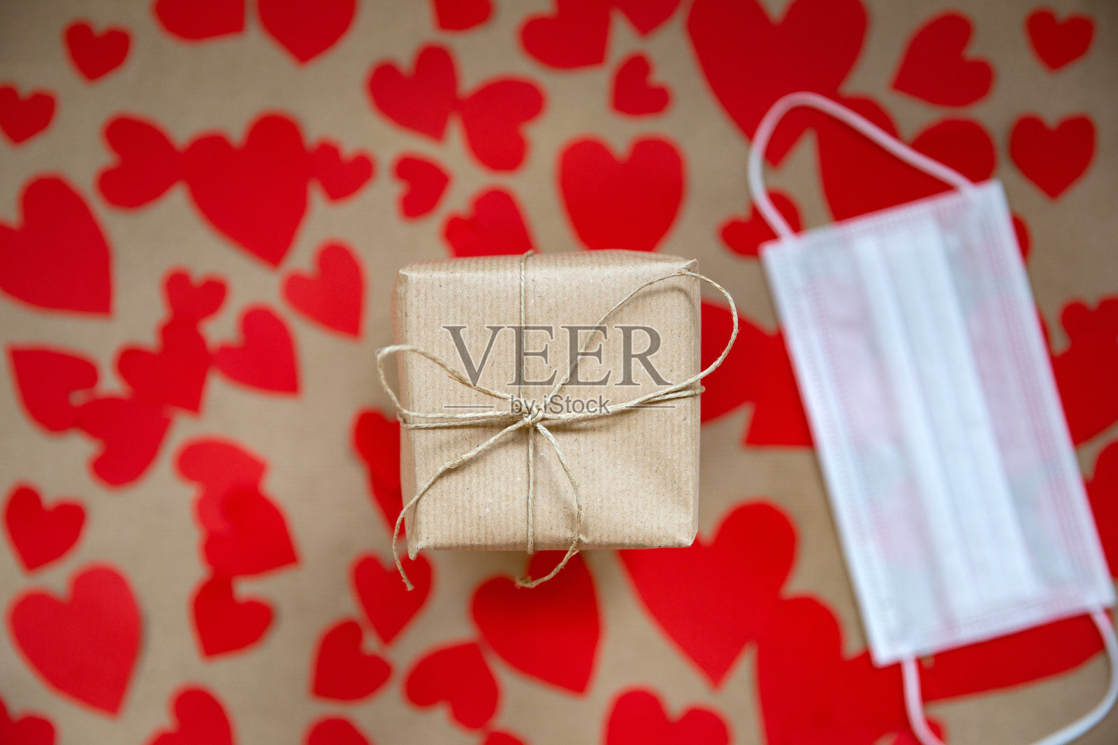 女性手握牛皮纸包裹的情人节礼盒，浪漫的红心和医疗面具的背景为冠状病毒，Covid-19和假日，情人节，生日概念。照片摄影图片