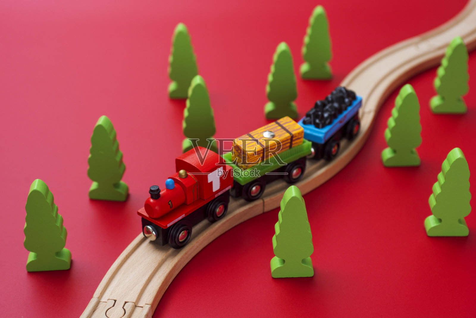 红色背景的绿树之间的铁路上的木制玩具火车。学龄前和幼儿园儿童的教育玩具。照片摄影图片