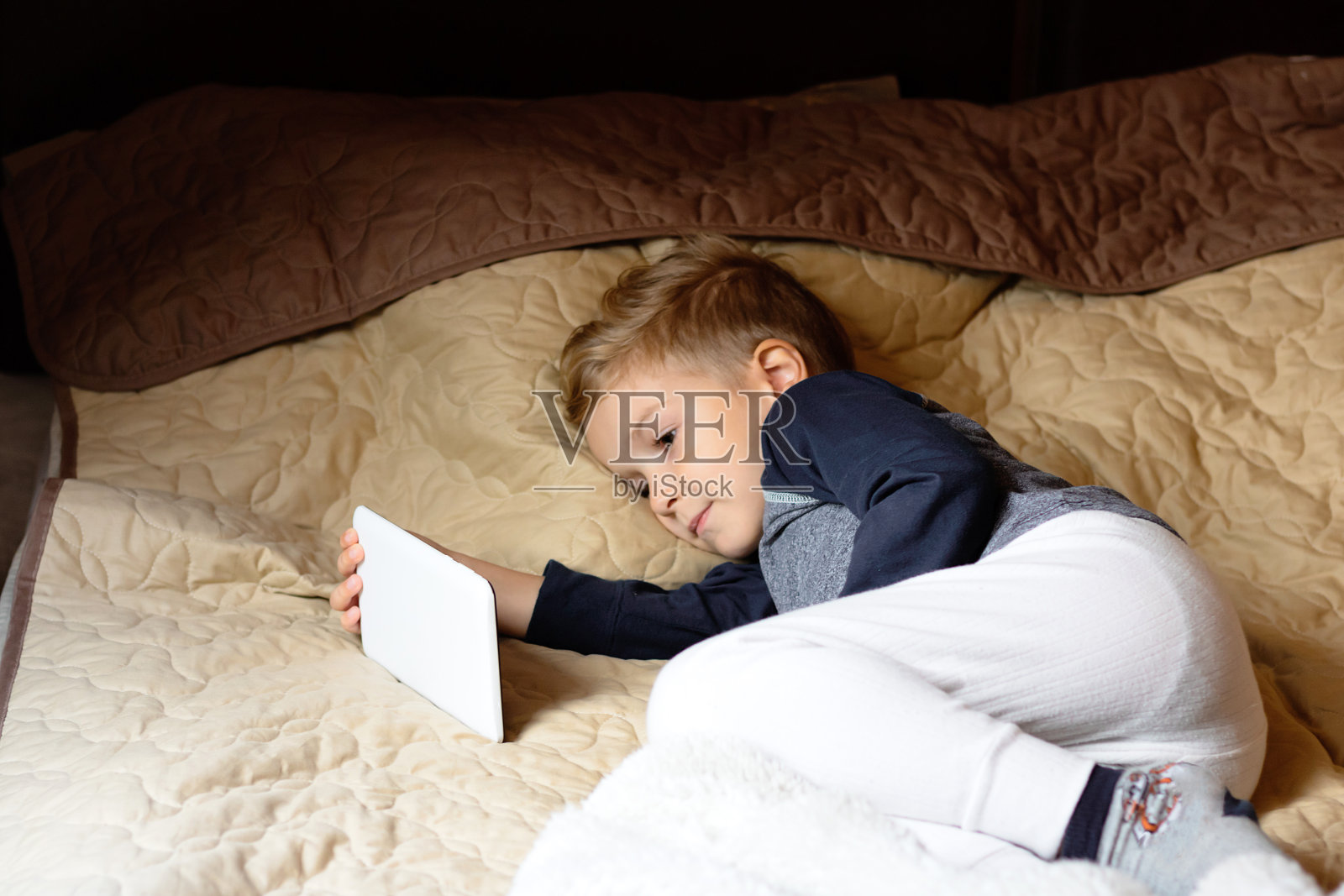 小孩子在卧室里使用平板电脑。照片摄影图片