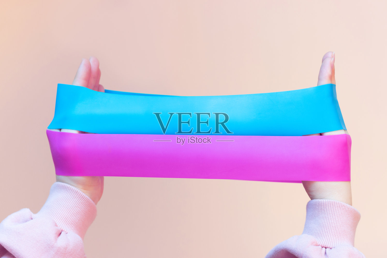 女孩拿着两个健身牙龈，粉红色背景上的扩张器，正面视图照片摄影图片