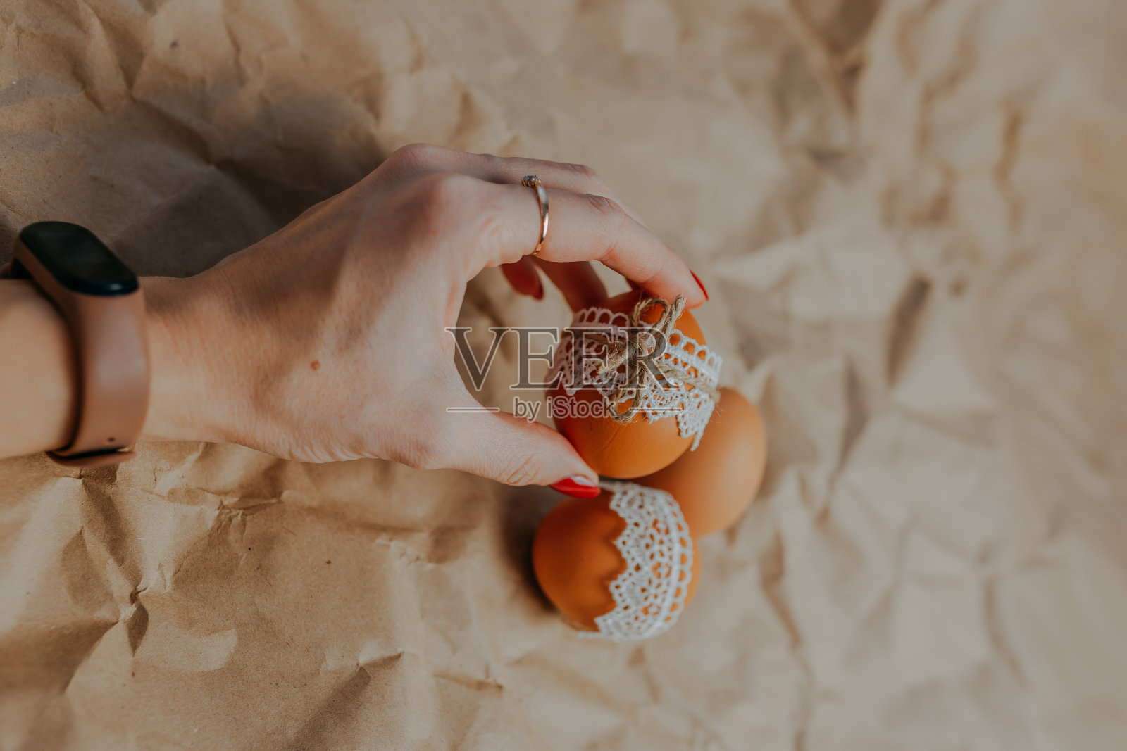 用花边和绳子在牛皮纸上装饰复活节彩蛋。三个复活节彩蛋在牛皮纸背景。女人手拿复活节彩蛋。照片摄影图片