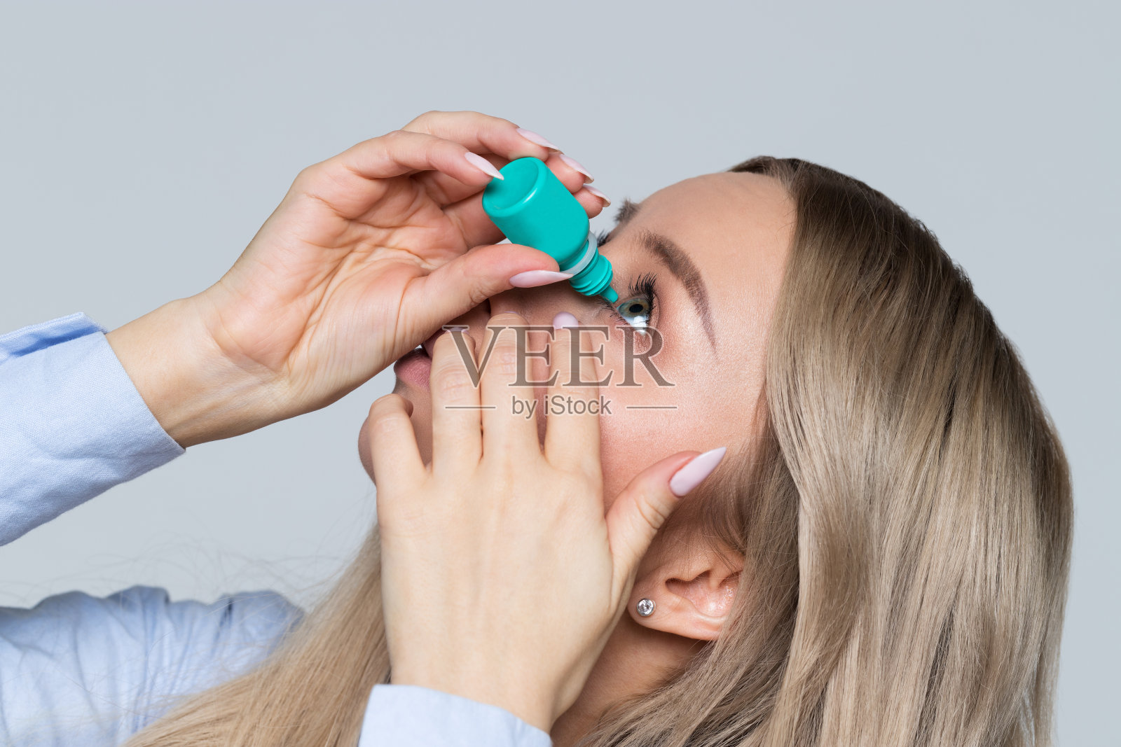 年轻女子滴眼液的特写，灰色背景，孤立。眼睛干涩照片摄影图片