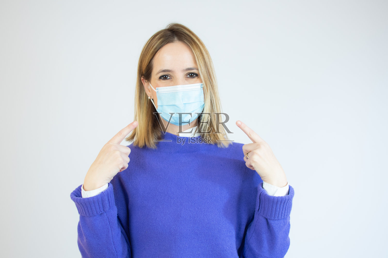 戴着外科口罩的妇女在白色背景下竖起手指。照片摄影图片