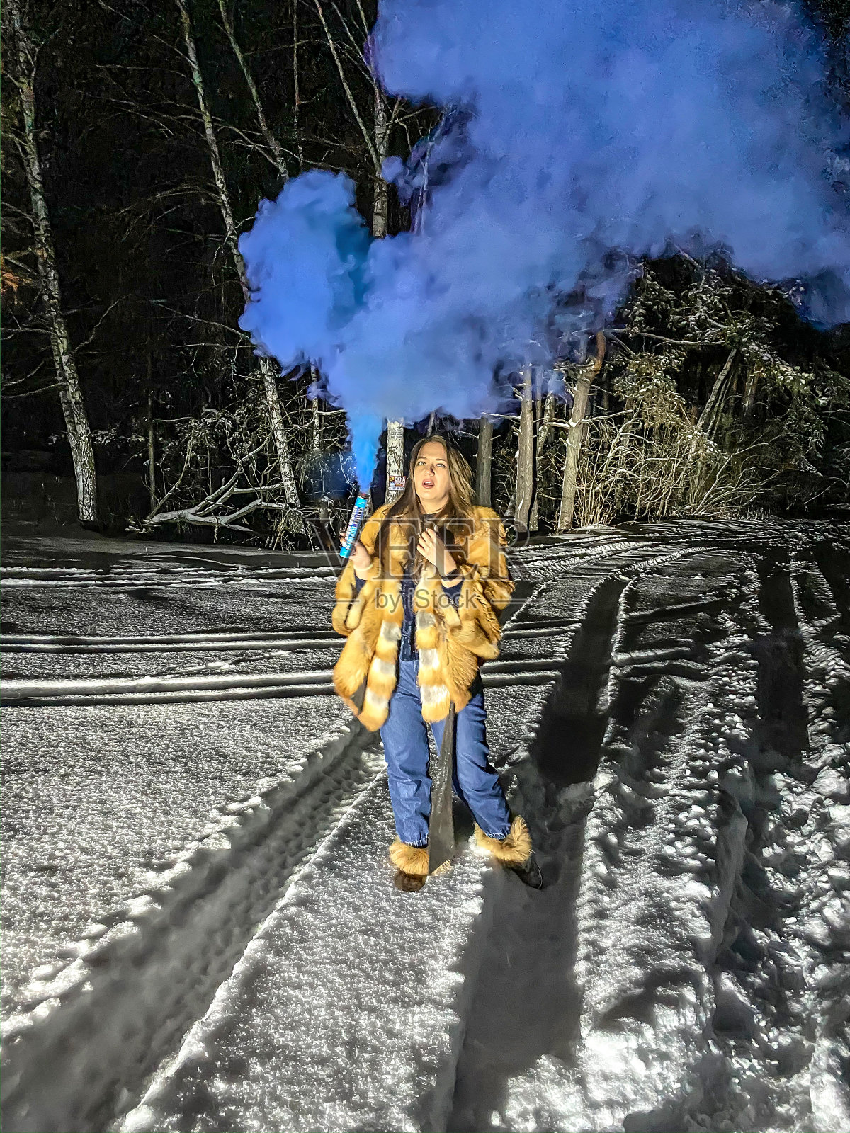 在冬天的森林里，一个年轻的女人在夜晚的雪地里走着，带着蓝色的烟雾照片摄影图片