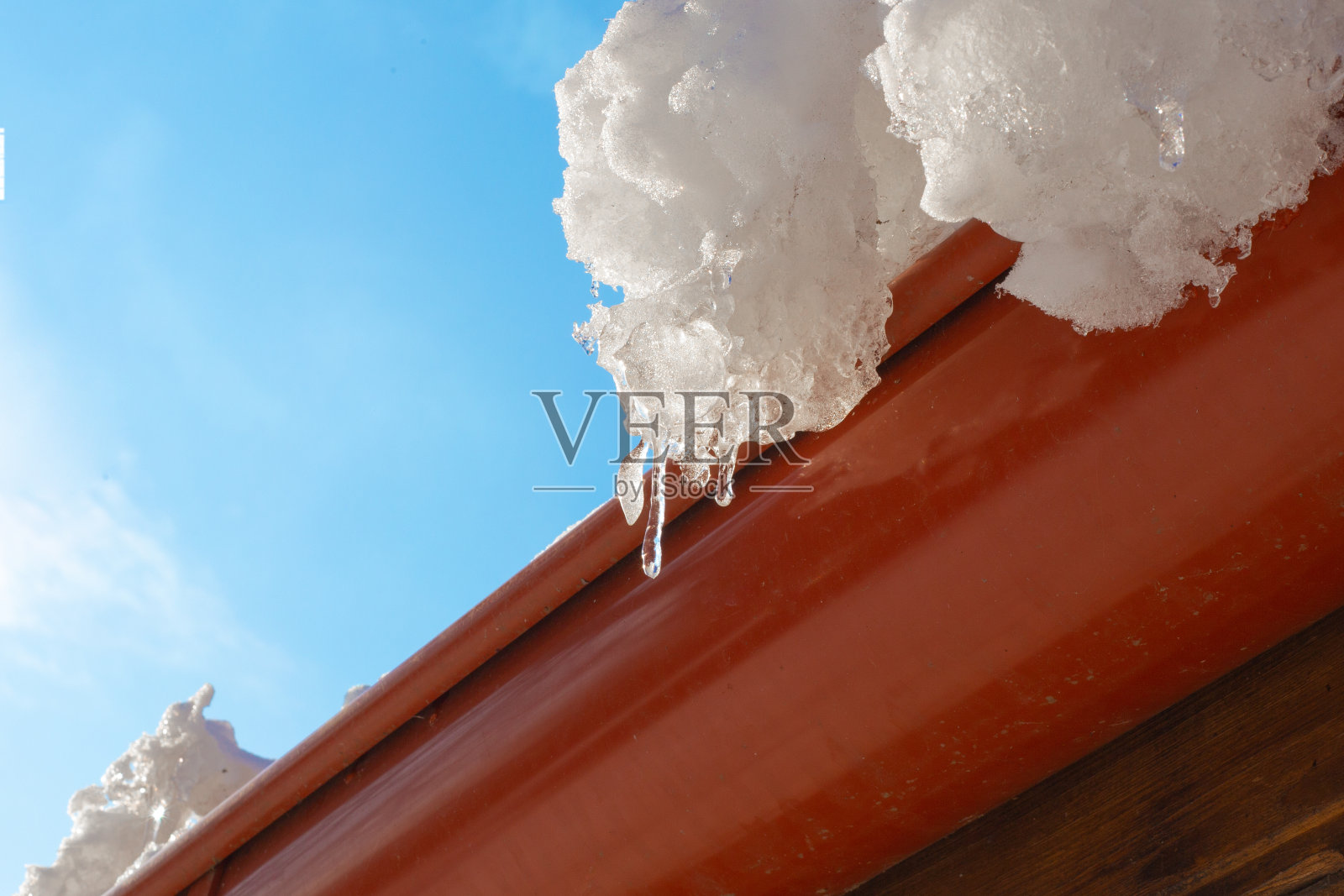 在一个阳光明媚的春日，屋顶上挂满了冰柱，映衬着蔚蓝的天空照片摄影图片