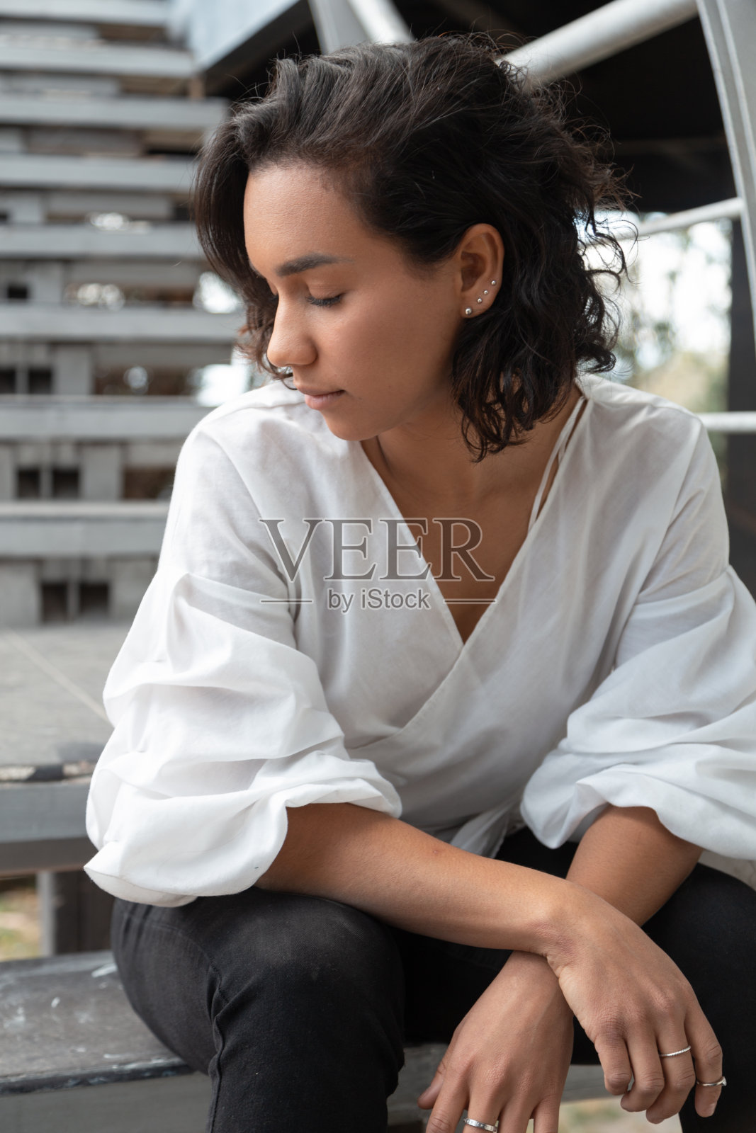 优雅的拉丁年轻女子留着短发，坐在楼梯上，穿着白色衬衫，黑色长裤和靴子，天照片摄影图片