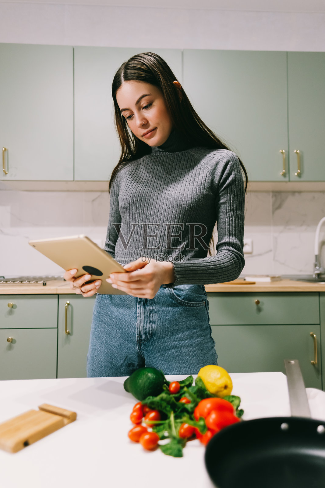 年轻女子在厨房里使用平板电脑，准备沙拉，阅读食谱。照片摄影图片