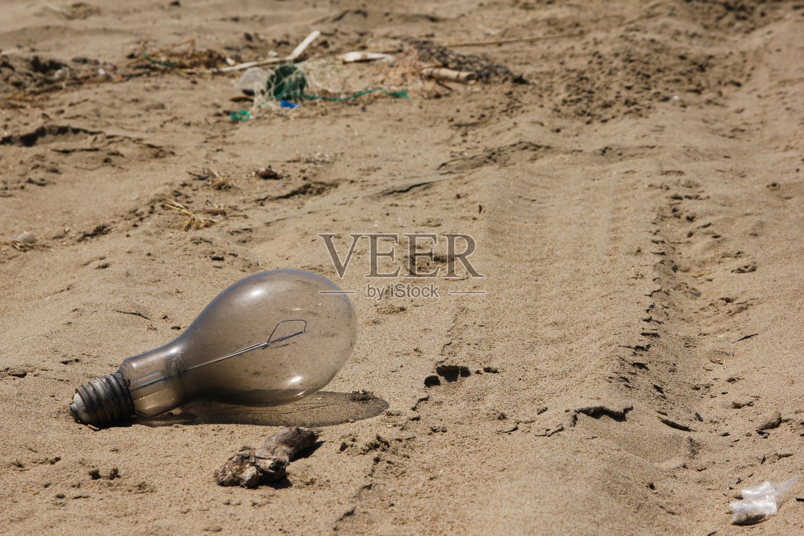 一个旧灯泡的细节躺在肮脏的海滩上。照片摄影图片