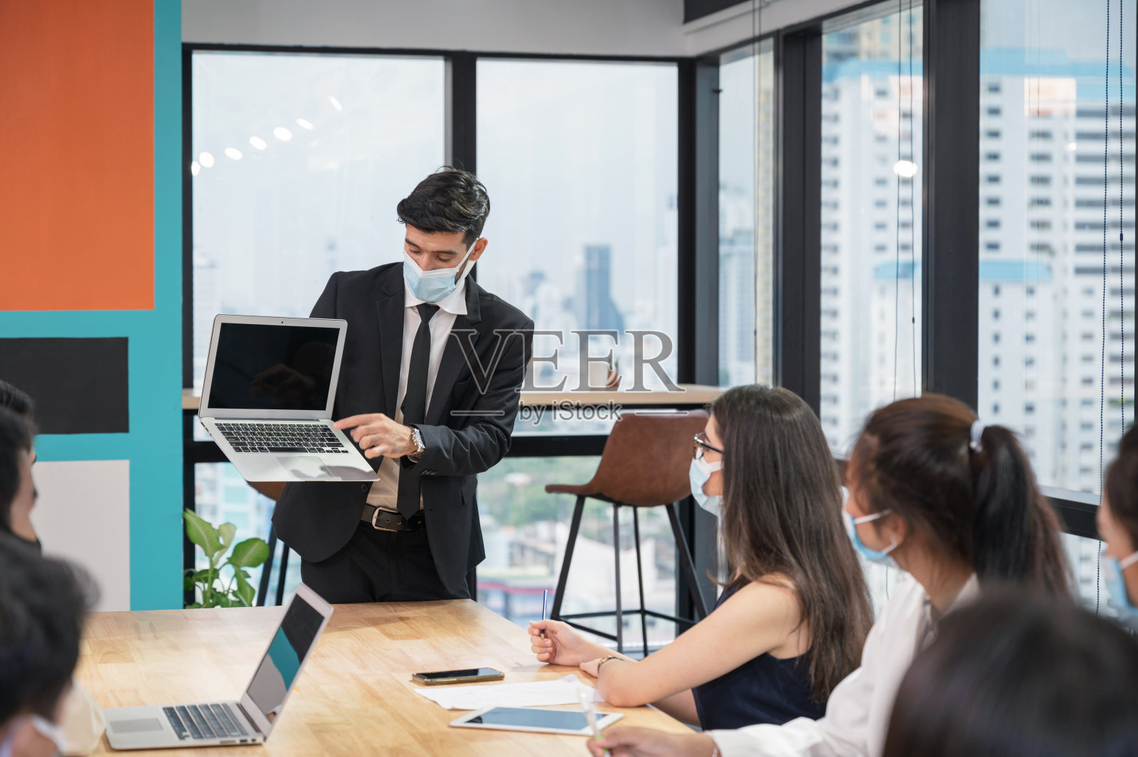 商务人士戴口罩，在现代办公环境中，在笔记本电脑上展示商务计划照片摄影图片