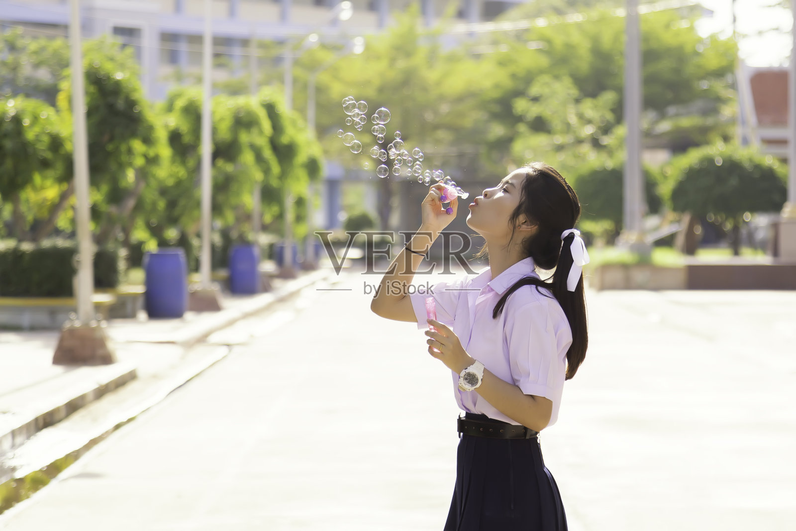 穿着校服的少年微笑着站在学校的街道上，泡泡到处飘。夕阳西下，泰国学生在微笑。照片摄影图片