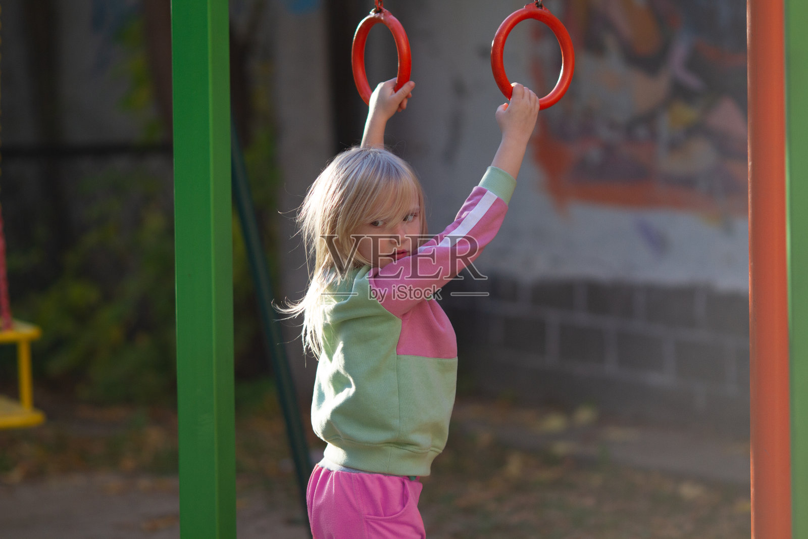 可爱的金发蹒跚学步的女孩穿着花哨的运动服在户外体操环在一个阳光明媚的日子照片摄影图片