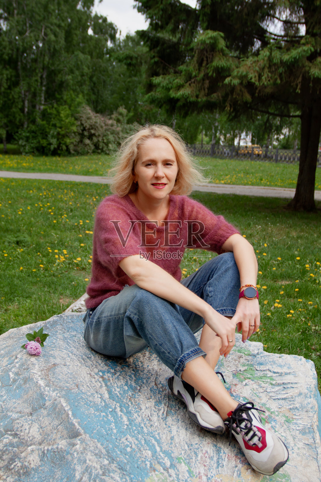 漂亮的金发女人坐在公园的巨石上，在漫长的散步后放松，辛苦的一天照片摄影图片