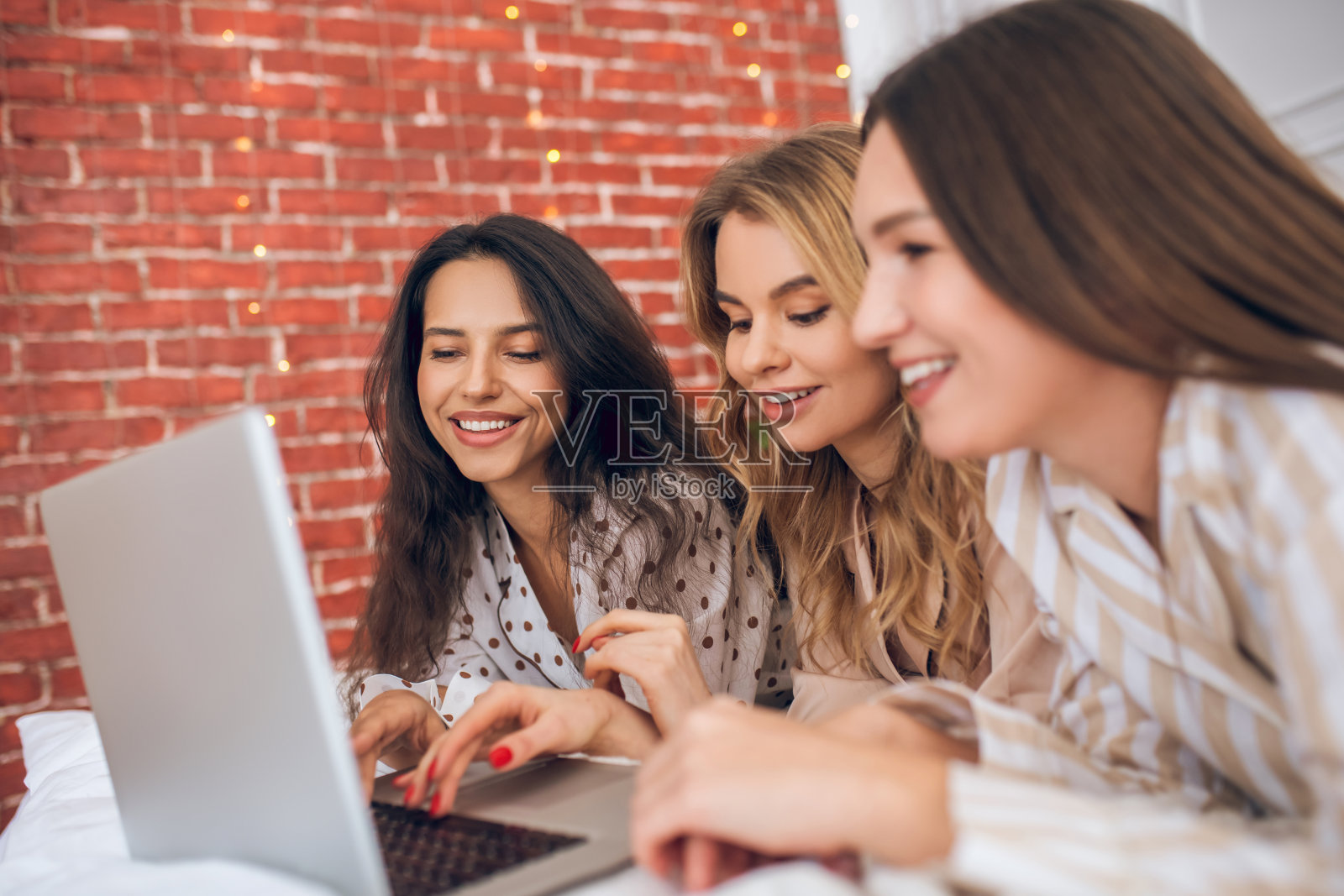 三个女孩躺在床上看笔记本电脑照片摄影图片