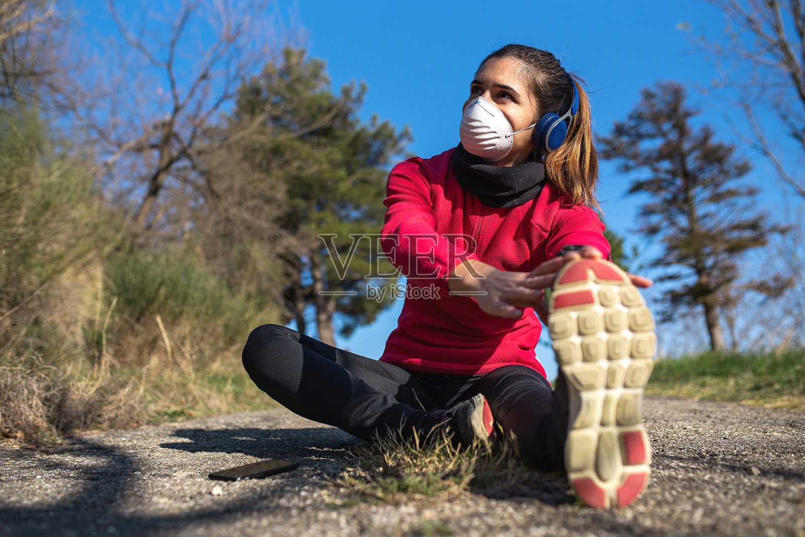 戴耳机的妇女戴着防护口罩在户外伸展以防止冠状病毒污染照片摄影图片