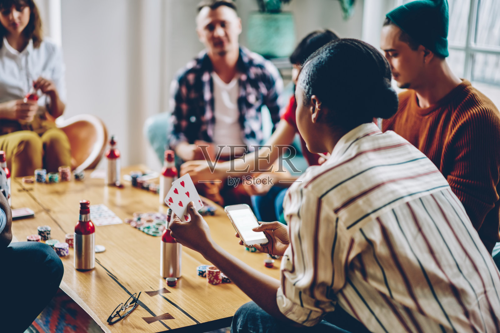 后视图的非洲裔美国嬉皮士女孩与扑克使用模拟智能手机小装置与空白屏幕赌场博彩广告，女性玩家聊天通过手机在友好的聚会照片摄影图片