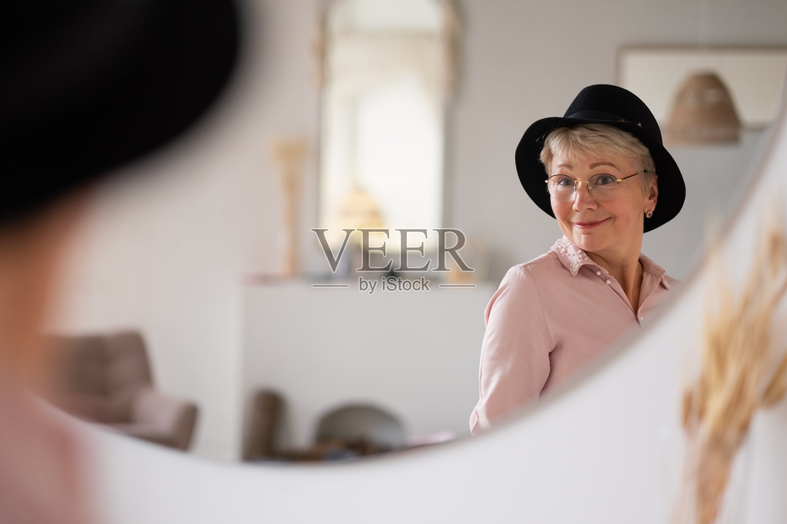 一名白人妇女在家试帽子看着镜子准备走路。照片摄影图片