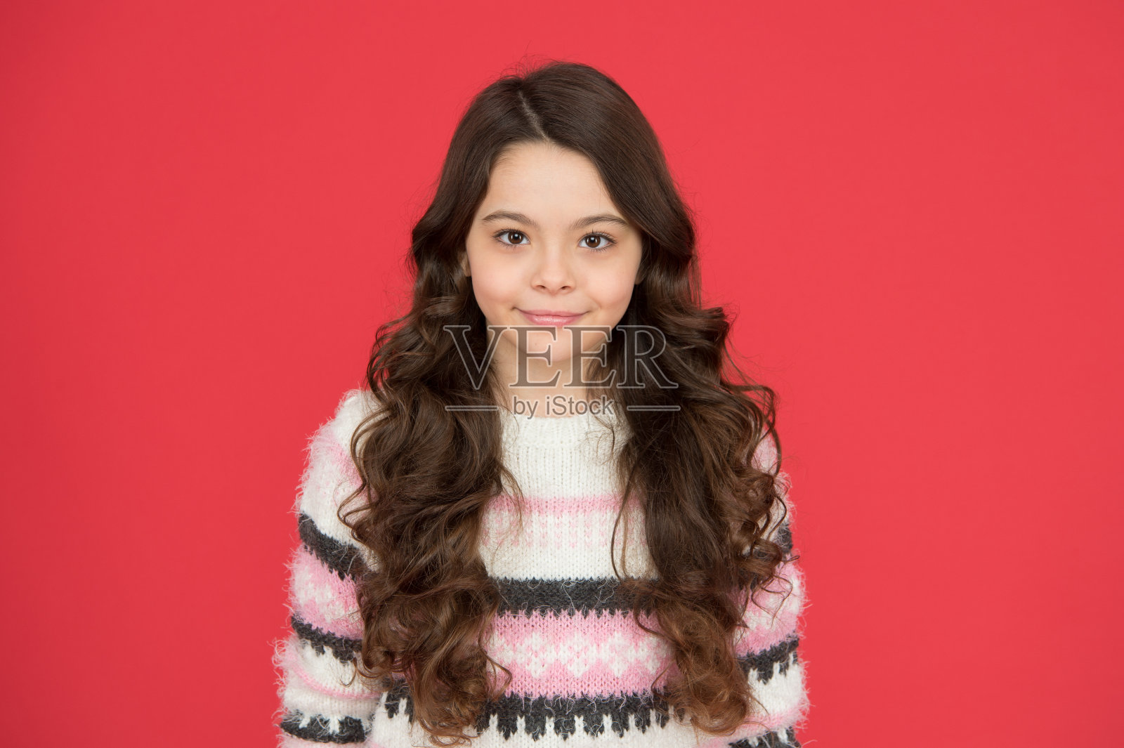 她的头发看起来是最好的方式。快乐的女孩与流动的头发红色背景。小孩儿微笑着，头发卷曲。小模特的美丽容颜。美发沙龙照片摄影图片