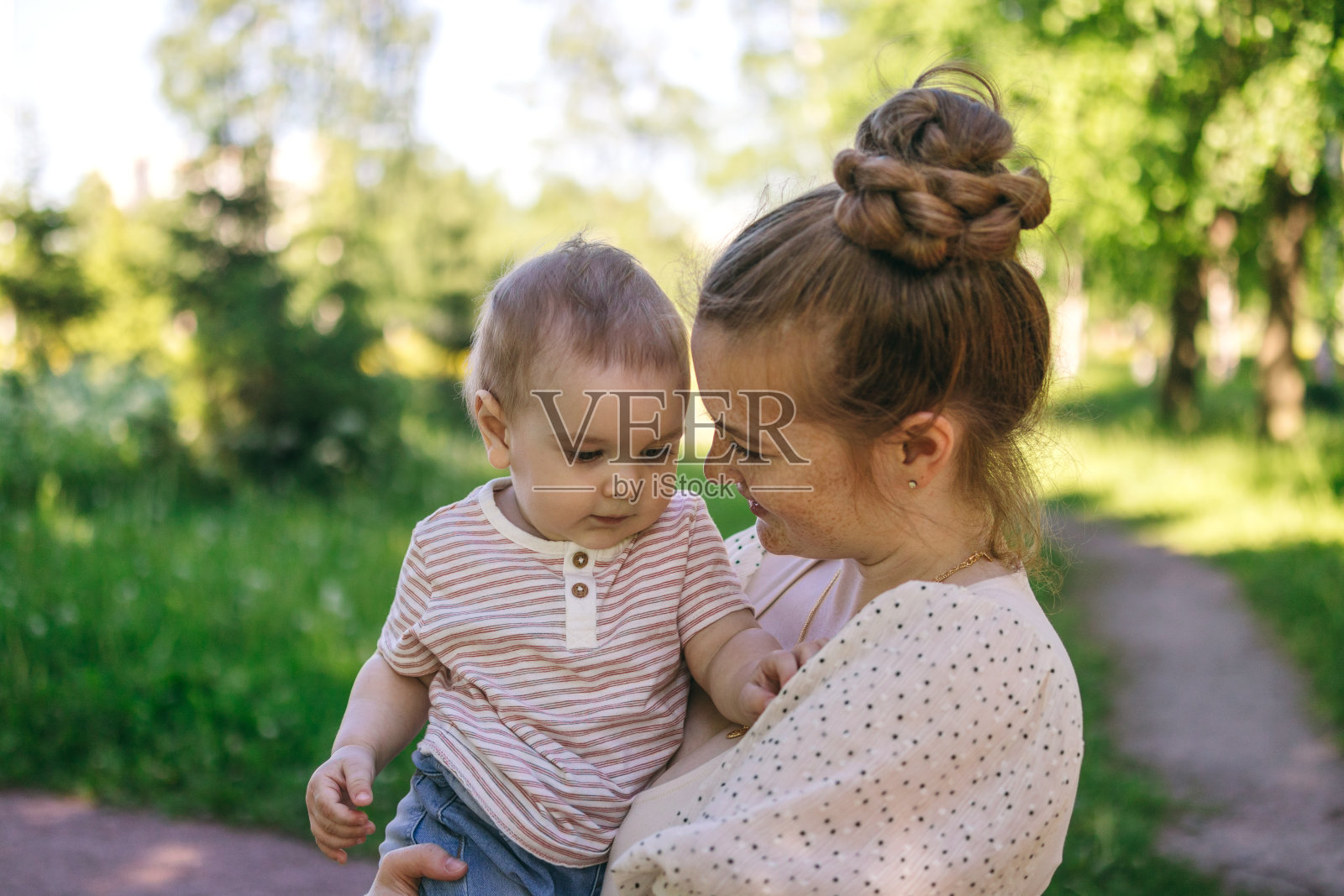 一个年轻的妈妈带着一个一岁的婴儿走，把他抱在怀里，拥抱。与孩子沟通，让他和谐发展照片摄影图片
