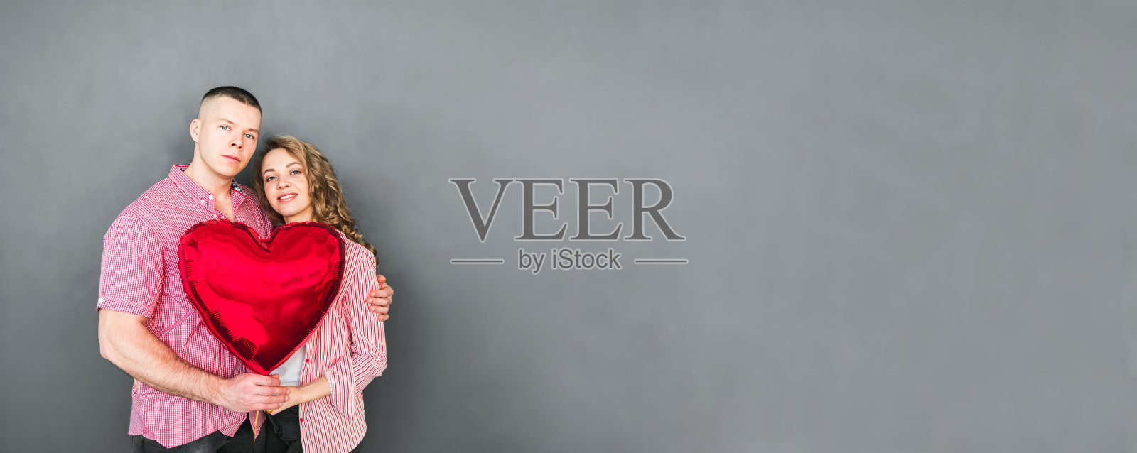 年轻的夫妇拥抱着，手里拿着一个红色的气球照片摄影图片