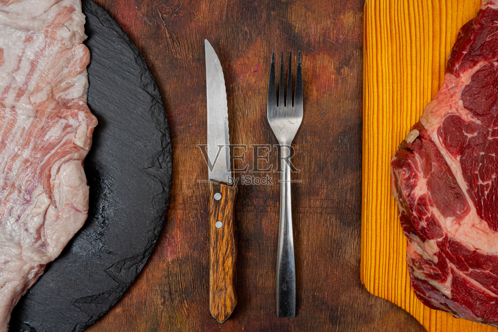 生牛排和猪肉秘密地放在一块木制的厨房板上，圆形的石板板放在一张棕色的旧木桌上照片摄影图片