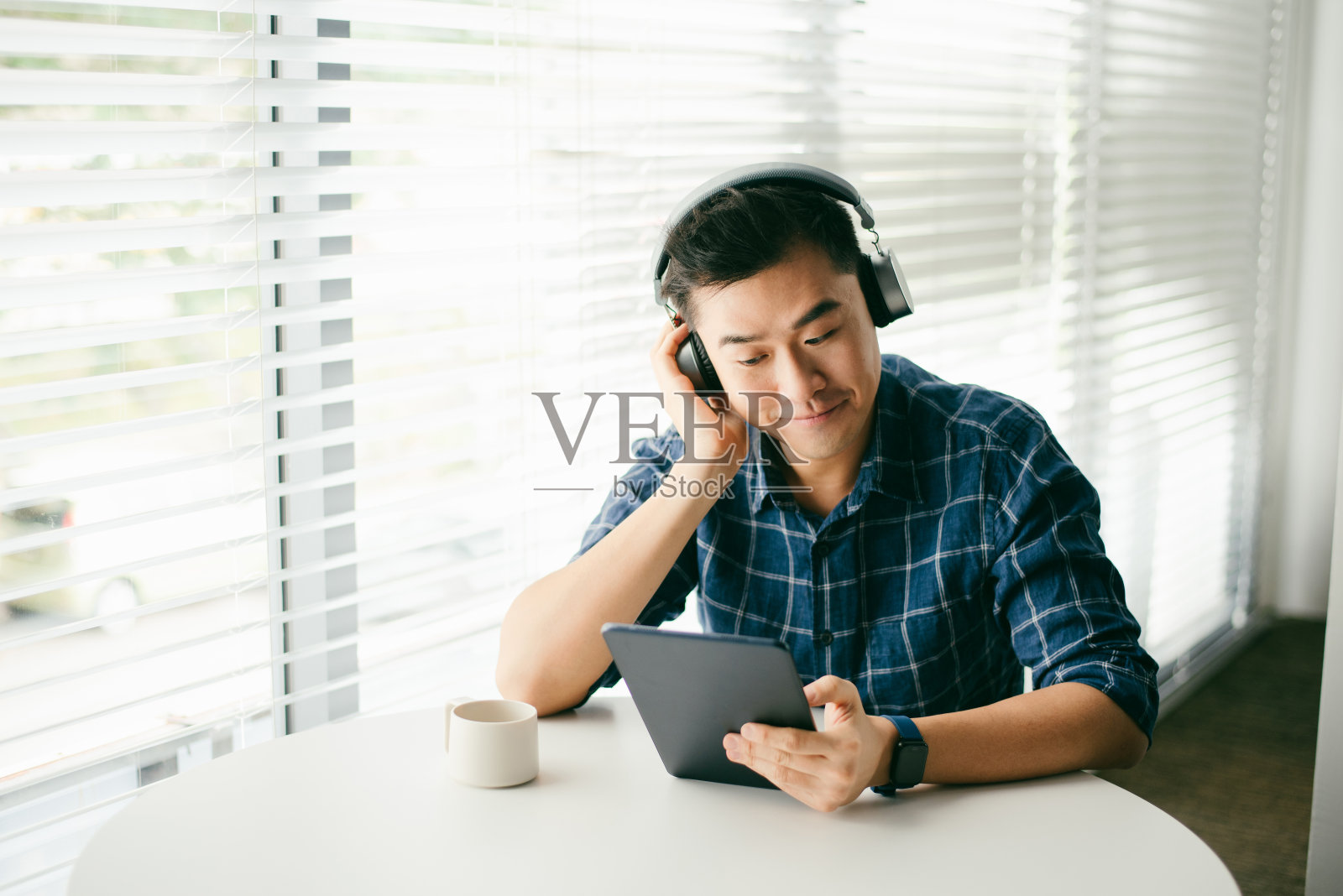 一名亚洲男子在客厅里使用无线耳机和平板电脑照片摄影图片