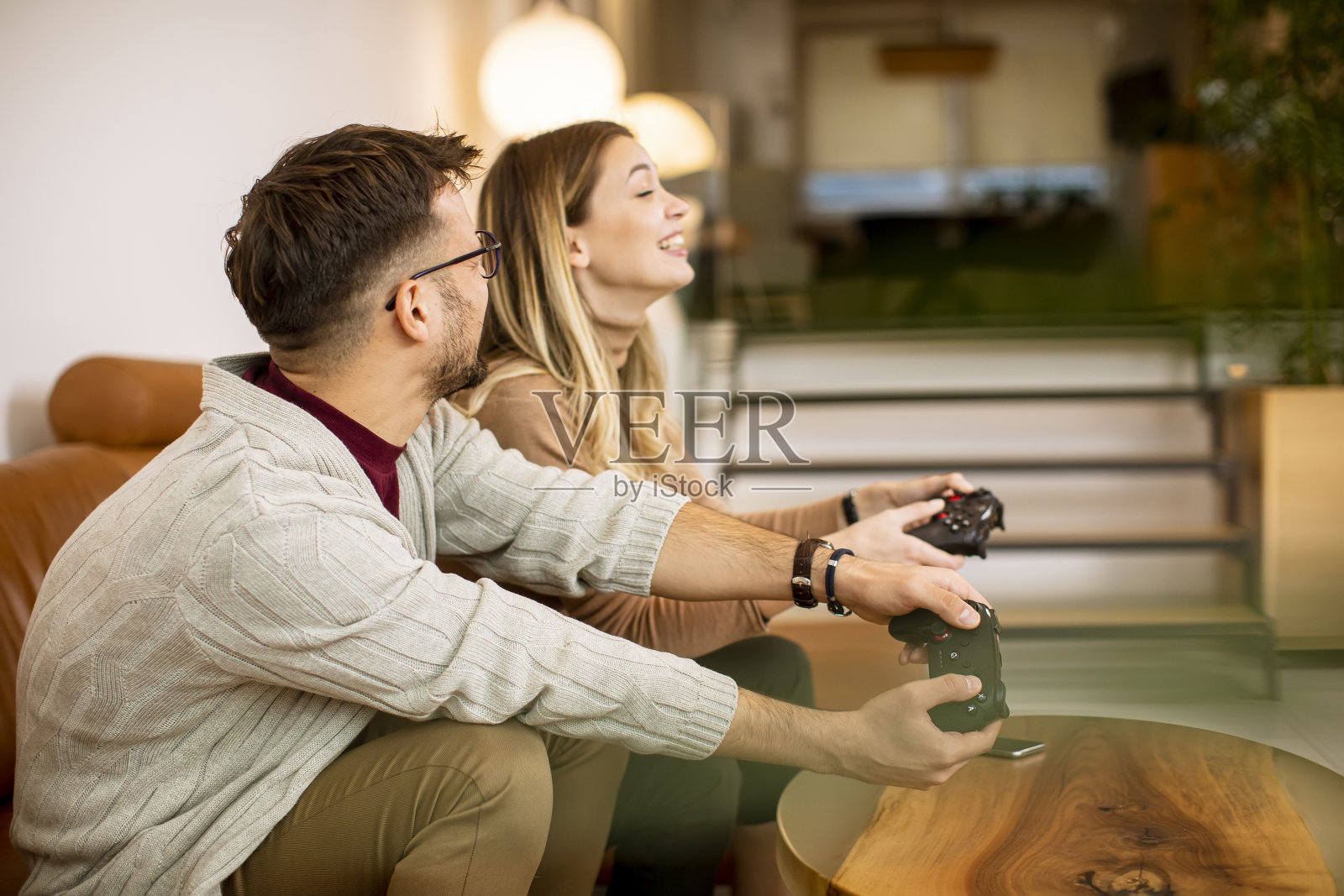 年轻夫妇在家里玩电子游戏，坐在沙发上玩得很开心照片摄影图片
