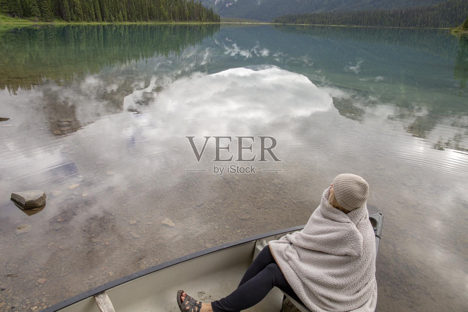 一个裹着毯子的女人坐在高山湖上的小船上照片摄影图片